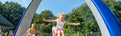 Twee blije kinderen springen en dansen op de interactieve Sona dansboog, een speeltoestel met geluid en spelletjes bij Bospark Lunsbergen in Drenthe.