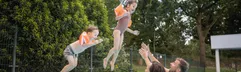 Twee kinderen met zwemvleugels springen in het buitenzwembad, waar hun ouders ze opwachten, op een zonnige dag bij De Katjeskelder.