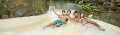 Een lachend gezin met twee kinderen glijdt samen van de brede familieglijbaan in het zwemparadijs Aqua Mundo bij Center Parcs De Kempervennen.