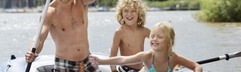 Een lachende vader met zijn twee kinderen in een opblaasbare boot op het zonnige Bostalmeer.