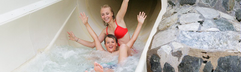Twee blije kinderen roetsjen samen met de armen in de lucht van de waterglijbaan in het Aqua Mundo zwemparadijs.