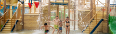 Kinderen en een volwassene worden natgespetterd door de reusachtige omkiepende emmer in het Water Playhouse van de Aqua Mundo op Center Parcs Port Zélande.