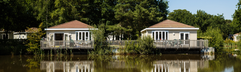 Twee luxe vakantiehuizen op palen direct aan het water van de recreatieplas op Molecaten Park De Flaasbloem, omgeven door groen.