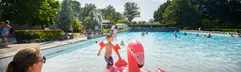 Een kind speelt met een opblaasbare roze flamingo in het buitengolfslagbad van Recreatiepark De Leistert op een zonnige dag.