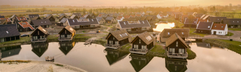 Luchtfoto van Dormio Resort Nieuwvliet-Bad bij zonsondergang, met een overzicht van de vele waterwoningen rondom het water en een zandstrandje.