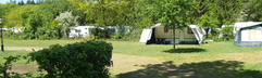 Ruime kampeerplaatsen met tenten en caravans in een groene, bosrijke omgeving op het vakantiepark.