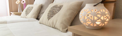 Een sfeervol opgemaakt bed met kussens en een nachtlampje in een van de comfortabele vakantiewoningen van Feriendorf Felsenhof.