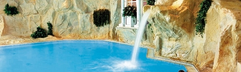 Het luxe binnenzwembad van Dorint Sporthotel Garmisch-Partenkirchen met rotswanden en een waterval waar gasten onder relaxen.