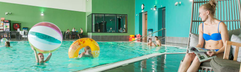 Een meisje zit aan de rand van het zwembad in het zwemparadijs van Landal Beach Resort Ooghdyne, terwijl andere kinderen in het water spelen.