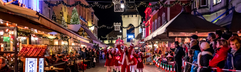 Dansende figuren in rode pakjes tijdens de kerstparade in een sfeervol verlichte straat met volle terrassen in Valkenburg.