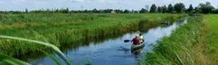 Twee mensen varen in een kano door een sloot in het natuurrijke landschap rondom Landal De Wedderplassen.