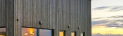 Stijlvolle moderne vakantiewoning van Landal Marissa aan het water tijdens zonsondergang, met sfeervolle verlichting en houten gevel.