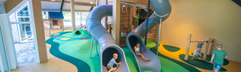 Kinderen glijden van de hoge, kronkelende tunnelglijbanen in het overdekte speelparadijs van Landal Orveltermarke.