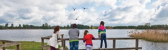 Gezin staat op een vlonder en kijkt uit over de grote recreatieplas met zandstrand bij Vakantiepark Landal Stroombroek.