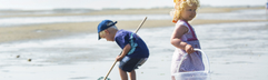 Jonge kinderen met een schepnetje en emmer zoeken naar krabbetjes en visjes in de branding op het strand van Terschelling.