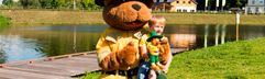 Bollo de Beer, de mascotte van Landal, geeft een high five aan een blij kind aan de oever van het meer op vakantiepark Wirfttal.