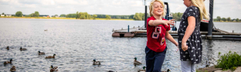 Twee kinderen staan aan de waterkant en voeren de vele eendjes die zwemmen in recreatieplas het Esmeer.