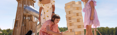 Kinderen spelen met reuze Jenga op het zandstrand van Vakantiepark Beekse Bergen, met een houten speeltoren op de achtergrond.