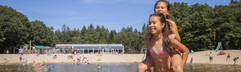 Twee lachende meisjes in badkleding spelen in het ondiepe water van het recreatiemeer bij het zandstrand van Bospark 't Wolfsven.