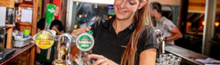 Vriendelijke medewerker tapt een drankje achter de bar in het restaurant van Vakantiepark De Bergen.