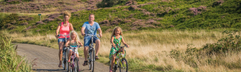 Een gezin met twee jonge kinderen fietst over een fietspad door het heuvelachtige duinlandschap van Texel.