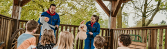 Een groep kinderen zit op strobalen te kijken naar een poppenkastvoorstelling door het animatieteam van Vakantiepark Dierenbos.