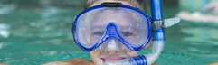 Een lachende jongen met een blauwe duikbril en snorkel kijkt in de camera vanuit het binnenzwembad van Ferienresort Cochem.