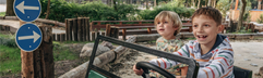 Twee lachende jongens rijden in een groene elektrische auto in het verkeerspark voor kinderen op Vakantiepark Kijkduin.