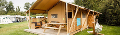 Een luxe houten safaritent (glamping) met veranda op een groen grasveld op een vakantiepark in Zeewolde, Flevoland.