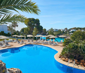 Het grote, lagune-stijl zwembad van Appartementen Esmeralda Park in Cala d'Or, omringd door ligbedjes en palmbomen.