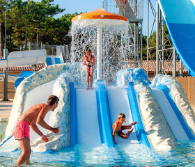 Jonge kinderen glijden van een brede kinderglijbaan met een watervalfontein in het peuterbad van Atlantic Club Montalivet.