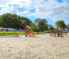 Een leuke speeltuin met een glijbaan, schommels en klimtoestellen, gelegen in het zand van het strand bij Bad Hoophuizen.