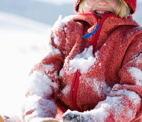 Een kind in een rode jas zit vol met sneeuw na het spelen en rollen in de diepe sneeuw tijdens een wintervakantie.