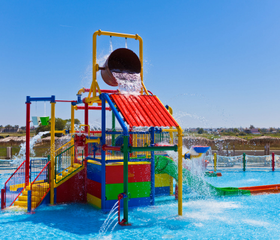 Een kleurrijke waterspeeltuin voor kleine kinderen bij Blue Lagoon Resort, met glijbanen en een grote omkiepende emmer die voor een waterval zorgt.