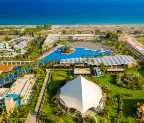 Een luchtfoto van het uitgestrekte Blue Lagoon Resort, waarop de zwembaden, de tuinen, de gebouwen en de ligging direct aan het strand van Kos te zien zijn.