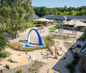 Overzicht van de centrale buitenspeeltuin en het terras bij Bospark Lunsbergen, met diverse speeltoestellen, zand en een interactieve Sona dansboog.