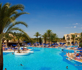 Zonnig overzicht van het lagune-stijl zwembad bij Bouganvilla in Sa Coma, met veel ligbedjes en gasten die genieten van het water.