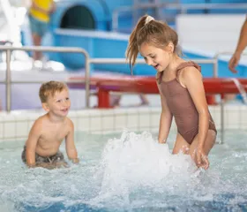 Twee jonge kinderen spelen en spetteren met water in het ondiepe peuterbad van het zwembad op Bungalowpark De Katjeskelder.