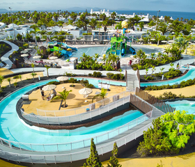 Bezoekers dobberen op een band in de lazy river van het Aqualava Waterpark, omringd door palmbomen.