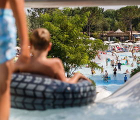 Kinderen op een opblaasband die van een brede waterglijbaan afglijden in het zwembad van Camping Altomincio Family Park.