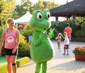 De groene kikker mascotte van Camping Altomincio Family Park begroet lachende kinderen samen met het animatieteam.