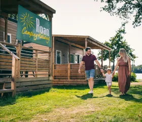 Gezin wandelt hand in hand voor hun houten stacaravan op een grasveld van Camping de Schatberg.