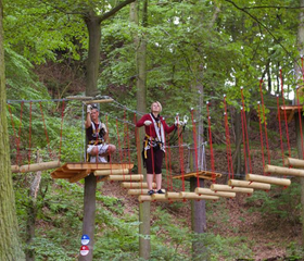Een meisje balanceert behendig over een touwbrug hoog tussen de bomen in het klimbos Kletterwald Eschwege.