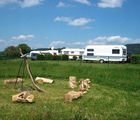 Ruime, groene kampeerplaats op Knaus Campingpark Eschwege met een kampvuurkring van houten stammen op de voorgrond.