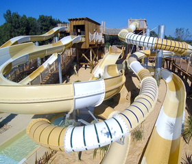 Overzicht van de vele kronkelende, geel-witte waterglijbanen en buizen in het grote aquapark van Camping Le Sérignan Plage.