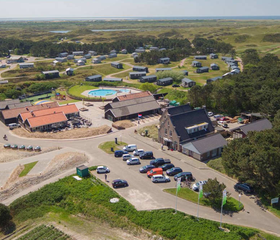 Een luchtfoto van Camping Loodsmansduin met het centrumgebouw en het buitenzwembad, gelegen in het duinlandschap van Texel.