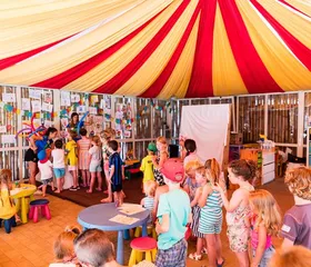 Kinderen doen mee aan creatieve activiteiten onder rood-gele circustent bij Camping Park Albatros