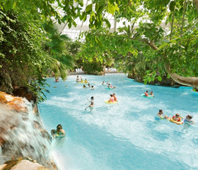Bezoekers laten zich op zwembanden meevoeren door de stroming van de wildwaterbaan, omringd door tropische planten in de Aqua Mundo van Center Parcs Bispinger Heide.