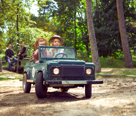 Twee kinderen rijden in een groene speelgoed-jeep over een bospad tijdens de Kids Safari bij Center Parcs De Kempervennen.
