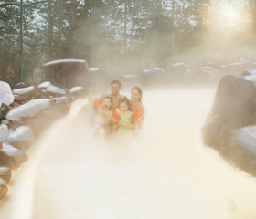 Een gezin geniet van het warme, stomende water in het buitenbad van de Aqua Mundo bij Center Parcs De Kempervennen, omringd door een besneeuwd landschap.